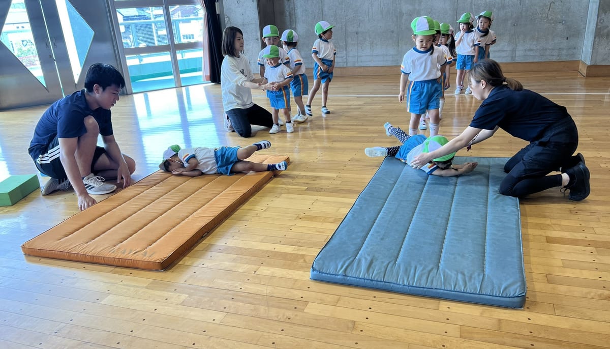 Children doing mat exercises in the activity hall, supported by their teachers