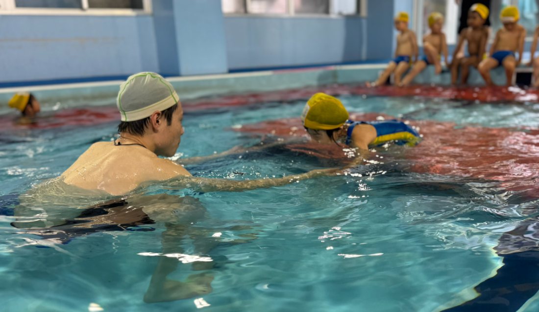 A child swimming in the indoor heated pool alongside a certified swimming teacher