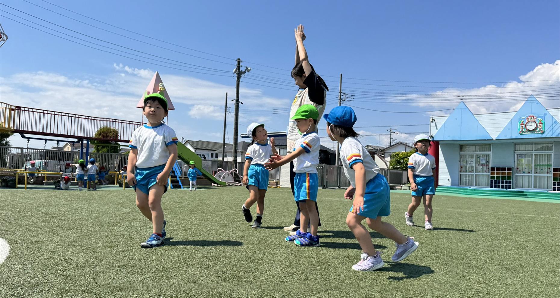 人工芝の園庭で先生といっしょに体を動かす厚木田園幼稚園の子どもたち